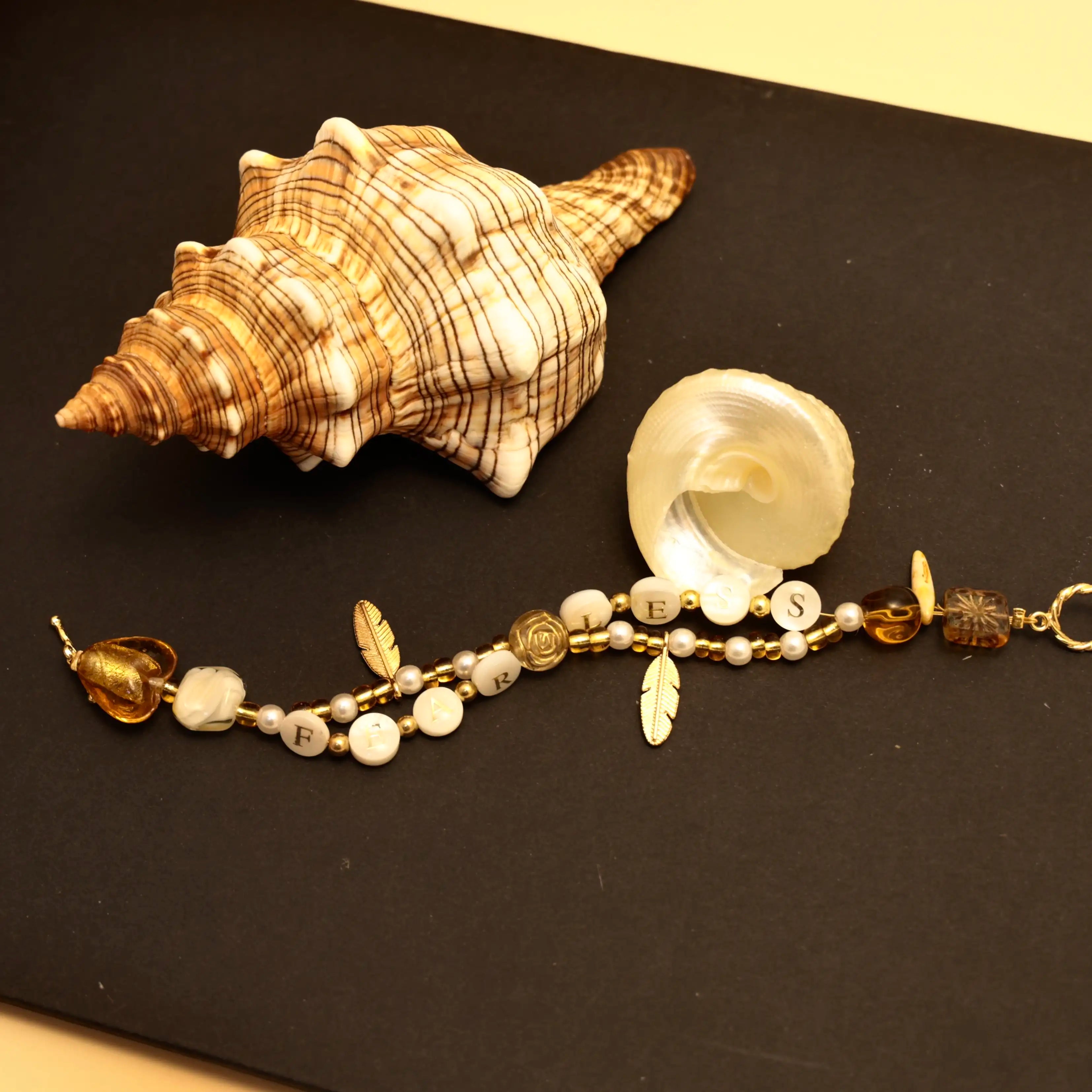 Flatlay of golden FEARLESS bracelet with seashells and soft light accents
