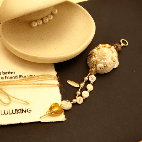 Golden bracelet wrapped around a seashell with pearl details and heart charm