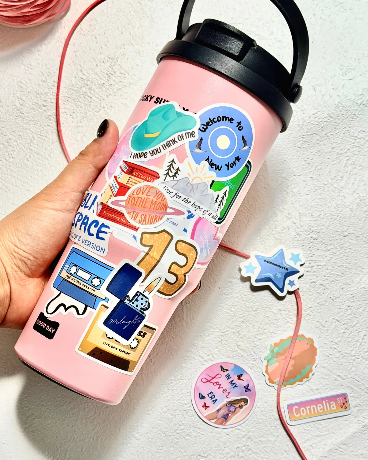 Pink insulated water bottle decorated with various era-inspired stickers, including 13 and midnights motifs.
