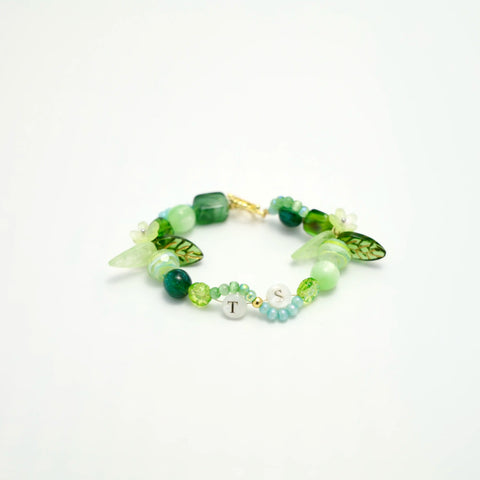 Flatlay of nature-inspired TS bracelet with green tones and floral charms