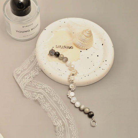Flatlay of the bracelet on a ceramic plate with lace and shell props, evoking a poetic mood