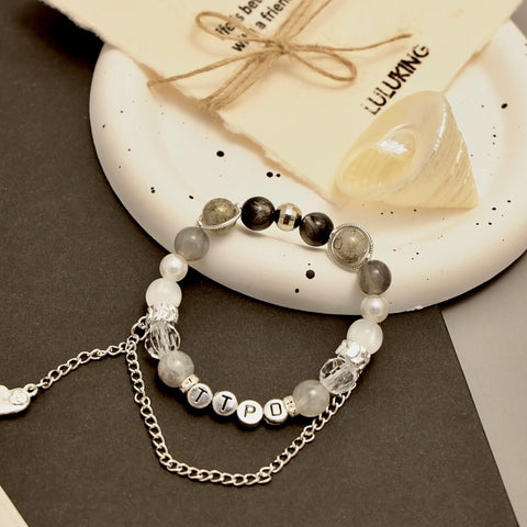 Artistic flat-lay of TTPD bracelet with LULUKING card, shell and lace